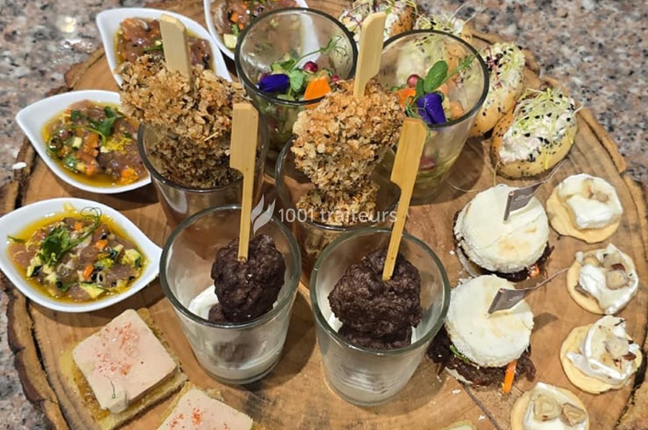 Plateau de dégustation varié avec verrines, toasts, bouchées salées et décorations colorées sur une planche en bois.