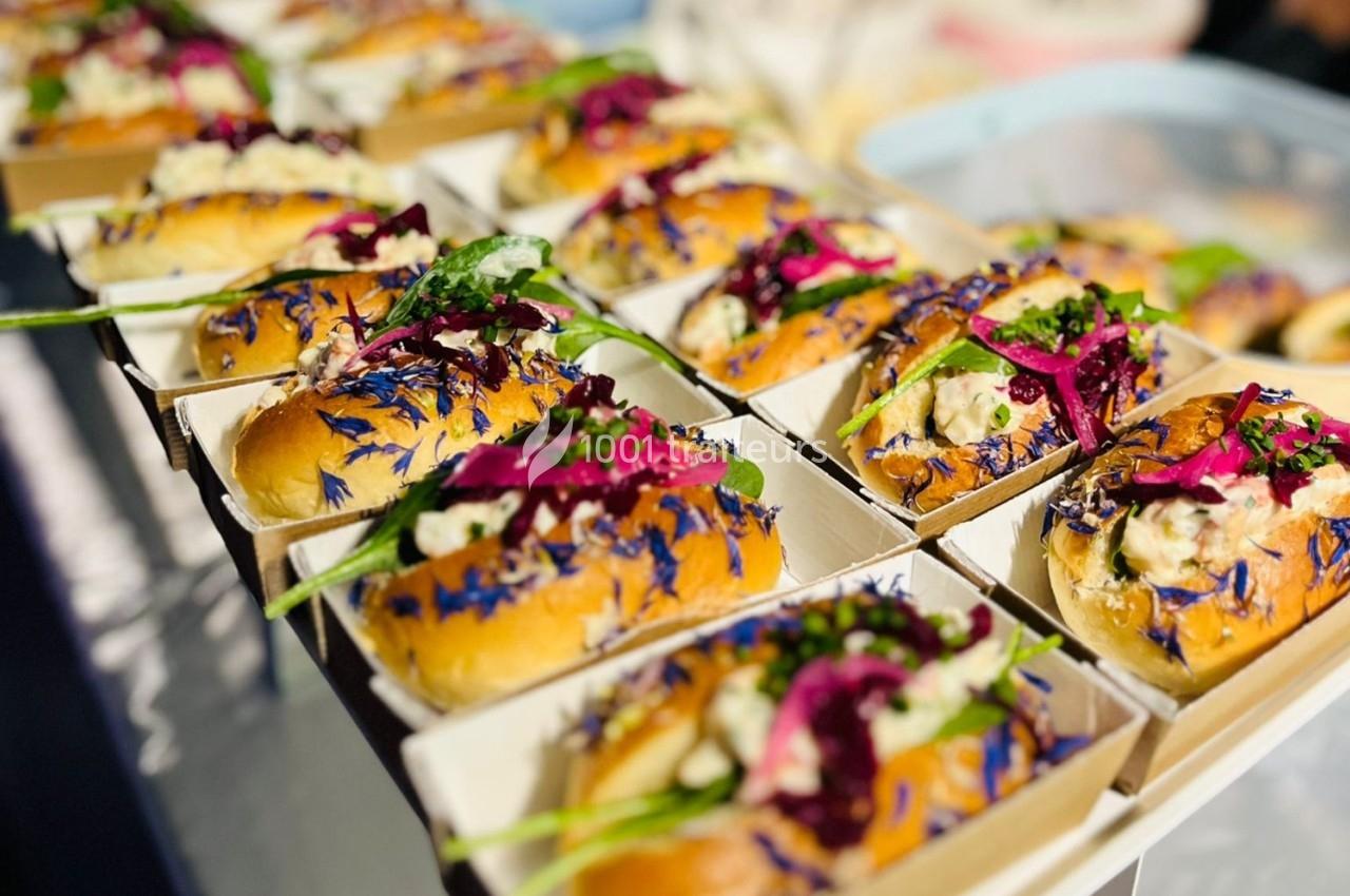 Petits pains garnis de salade, légumes colorés et fleurs comestibles, présentés dans des barquettes individuelles.