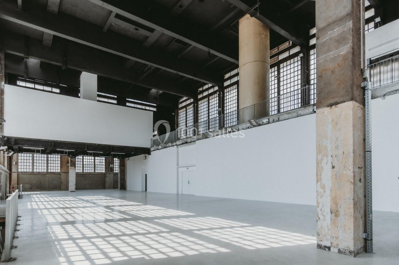 Intérieur d'un grand espace industriel vide avec des murs blancs, un sol en béton et de grandes fenêtres laissant entrer la…