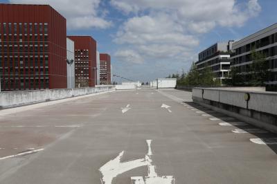 Vue d'un parking vide en extérieur, entouré de bâtiments modernes sous un ciel partiellement nuageux.