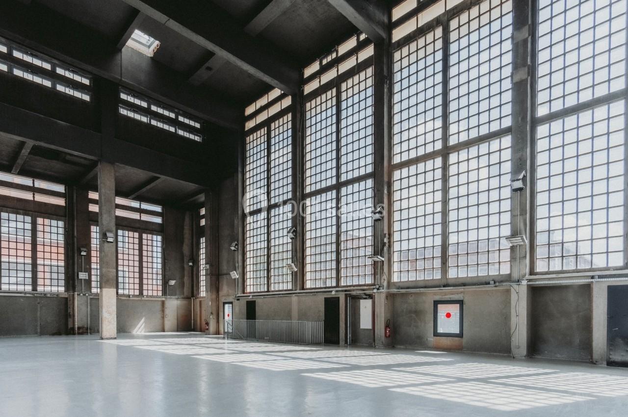 Intérieur d'un grand bâtiment industriel avec de hautes fenêtres en grille laissant entrer la lumière naturelle.