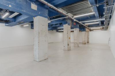 Vue d'un parking vide en extérieur, entouré de bâtiments modernes sous un ciel partiellement nuageux.