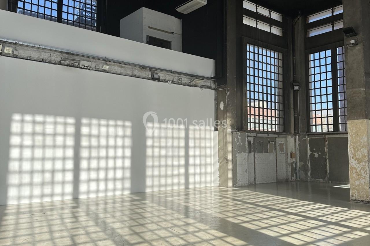 Intérieur d'une pièce industrielle avec de grandes fenêtres laissant entrer la lumière et des murs partiellement rénovés.