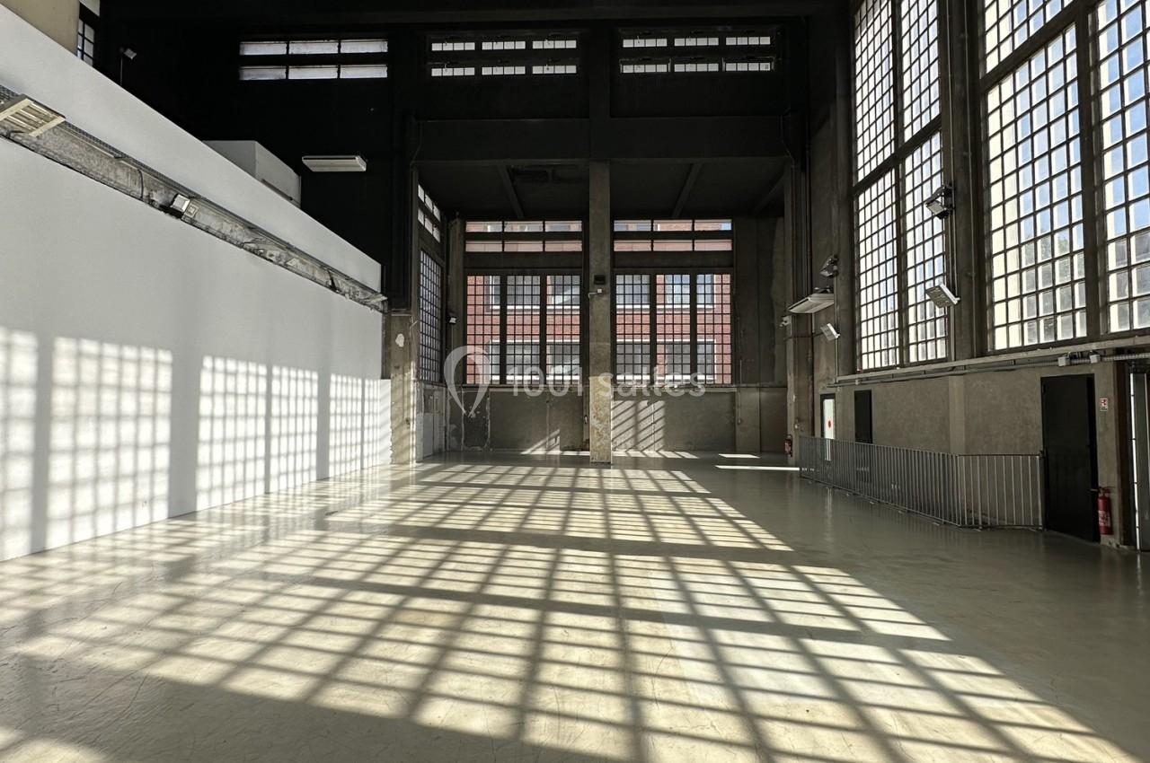 Intérieur d'un grand bâtiment industriel avec de larges fenêtres laissant entrer une lumière naturelle abondante.