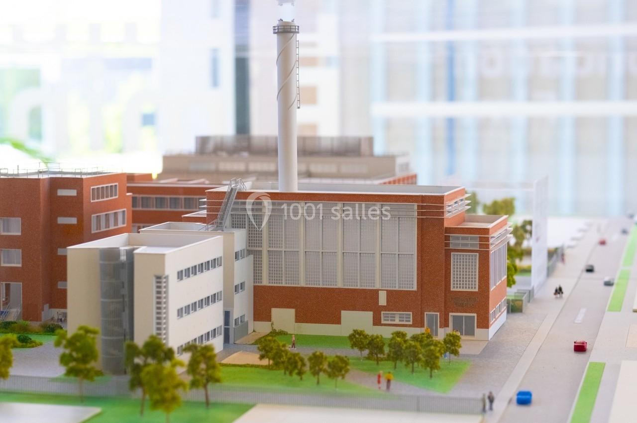 Maquette d'un complexe industriel en briques rouges avec une cheminée, entouré d'arbres et de rues.