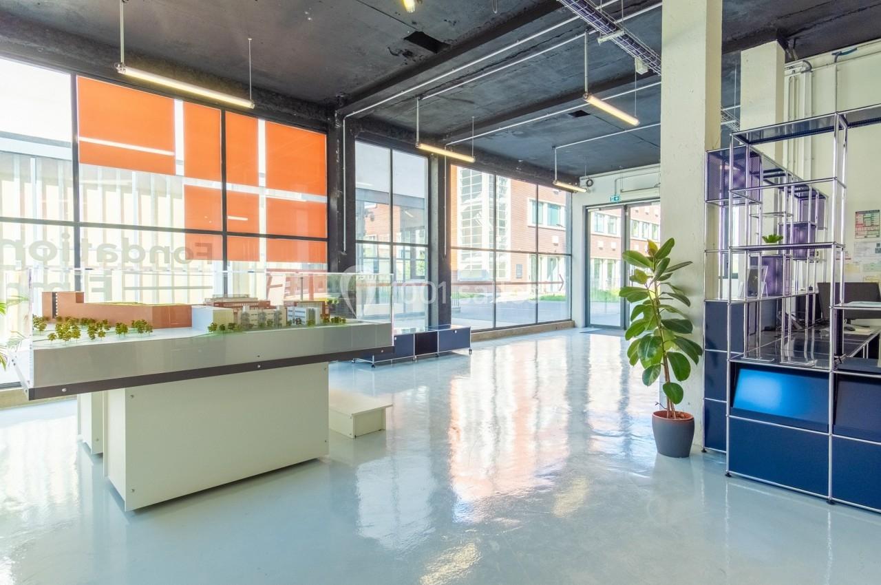 Intérieur lumineux d'un espace moderne avec maquettes sur une table, grandes baies vitrées et plantes décoratives.
