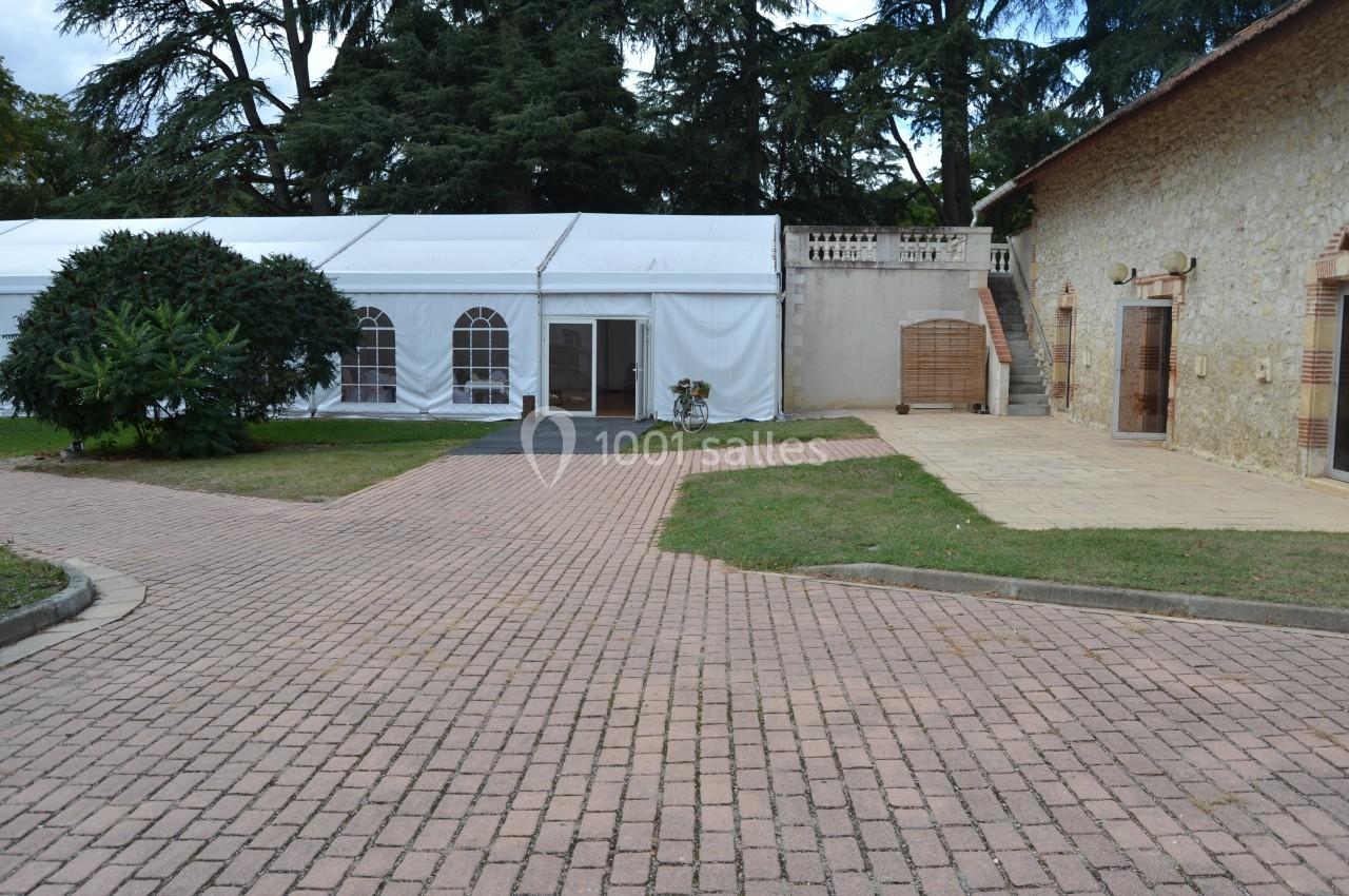 Cour pavée avec une tente blanche, un bâtiment en pierre à droite et des arbres en arrière-plan.