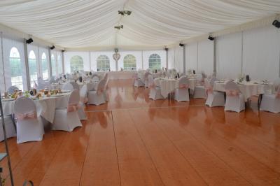 Décor de cérémonie en extérieur avec arche en bois, voilages blancs et verts, fleurs et chaises en bois.