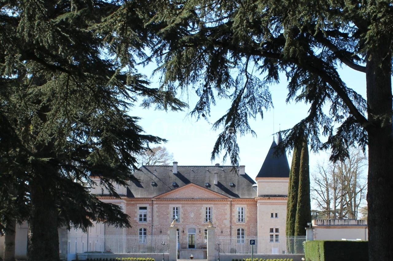 Allée bordée d'arbres menant à un bâtiment en pierre avec une tour, sous un ciel dégagé.