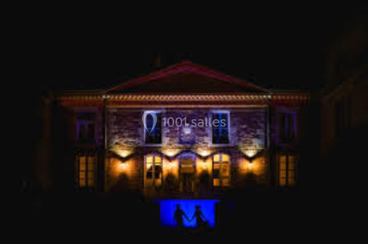 Façade d'un bâtiment éclairé par des lumières colorées, avec deux silhouettes se tenant la main au premier plan.