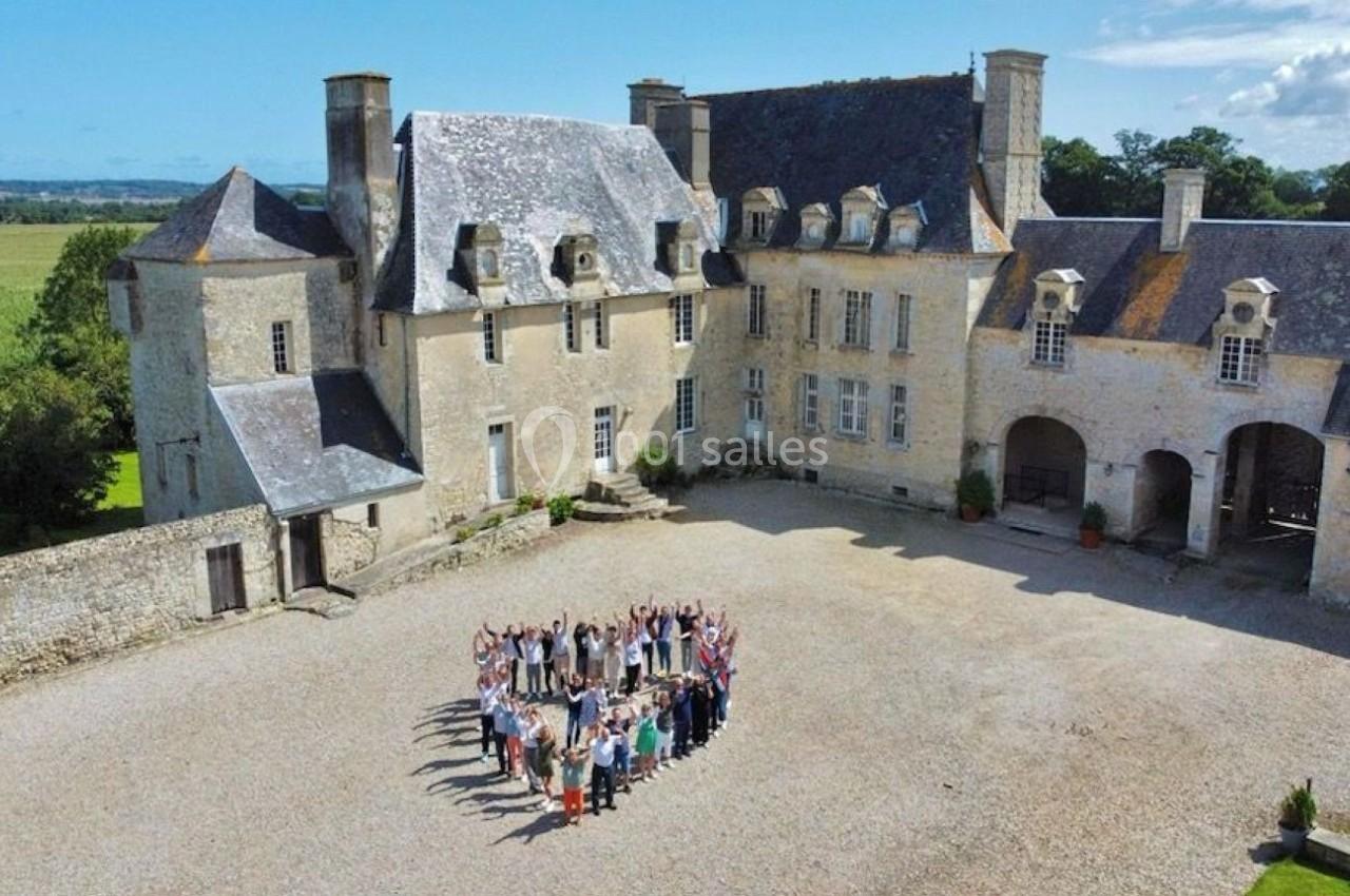 Un groupe de personnes formant un cercle dans la cour d'un château en pierre entouré de verdure.