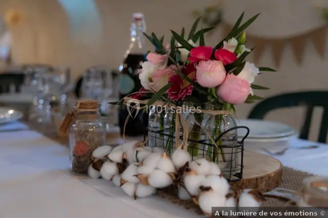 Centre de table avec bouquet de fleurs roses et blanches, branches de coton et décorations en verre sur une table dressée.