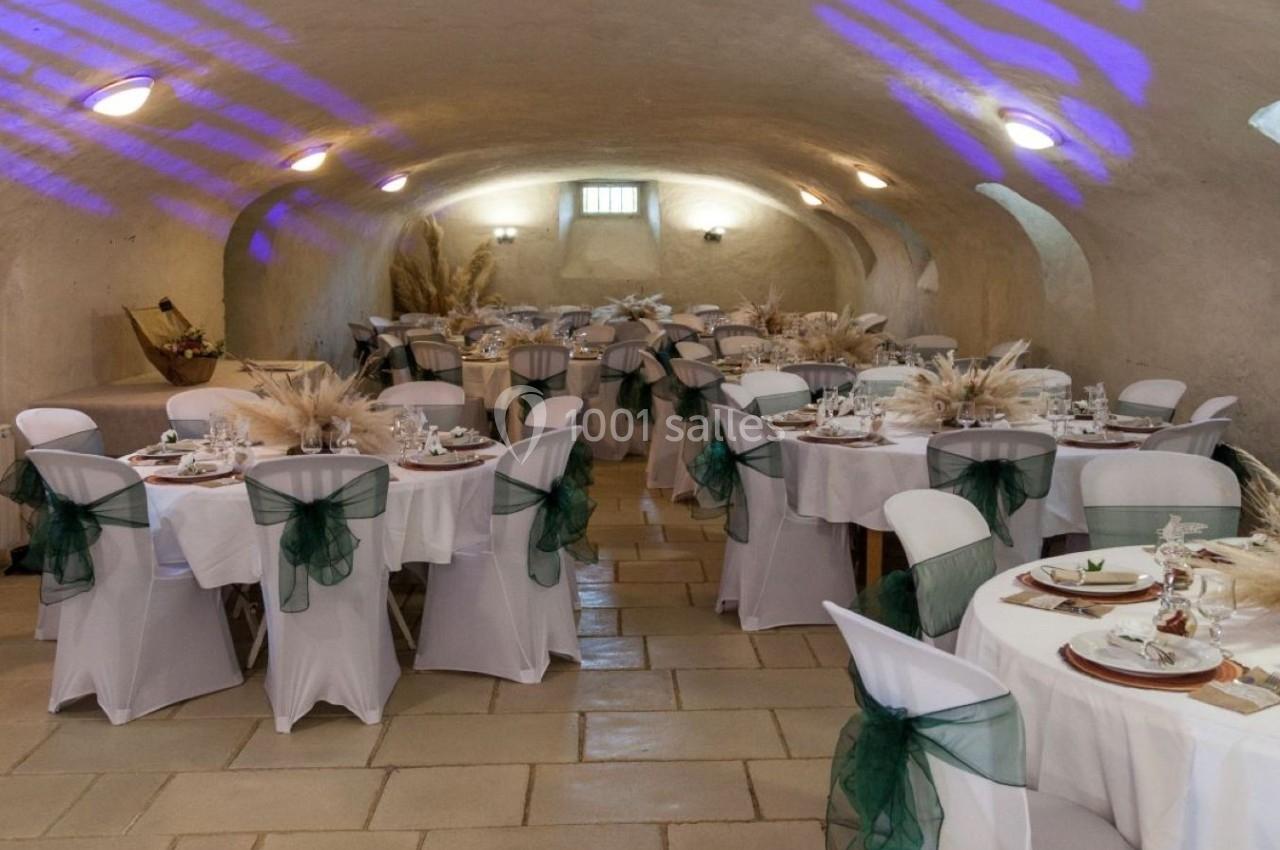 Salle voûtée décorée pour un événement, avec des tables rondes dressées et des chaises ornées de nœuds verts.