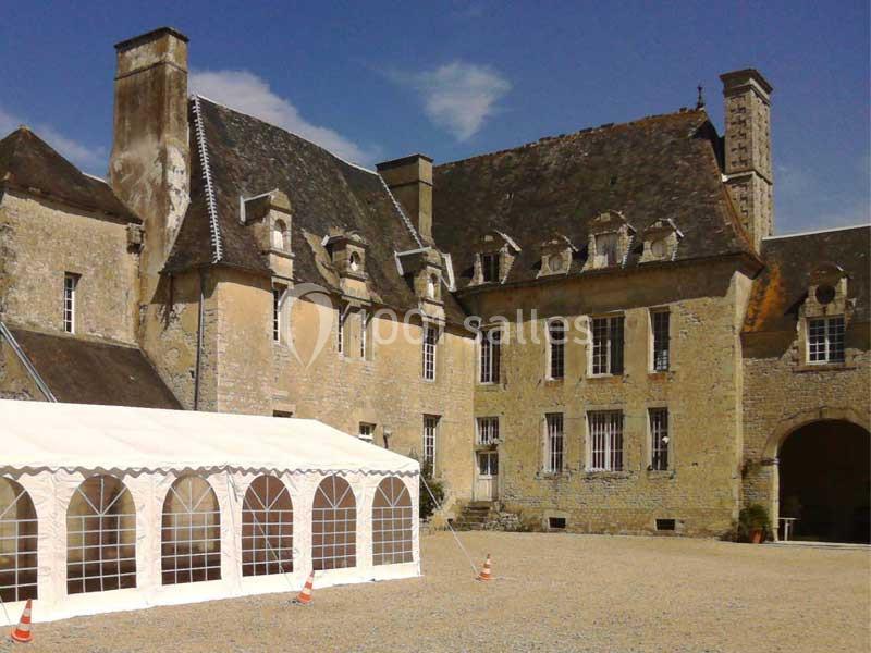 Façade d'un bâtiment ancien en pierre avec une grande tente blanche installée dans une cour gravillonnée.