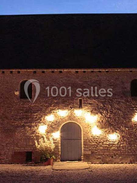 Façade en pierre éclairée par des appliques murales autour d'une porte en bois, vue de nuit.