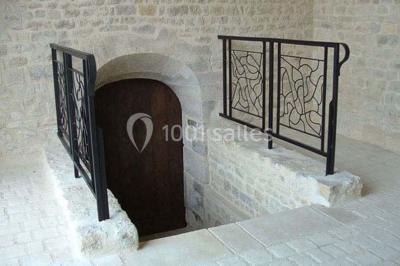 Cuisine rustique avec évier double, plan de travail en inox, réfrigérateur, cuisinière et mur en pierre apparente.