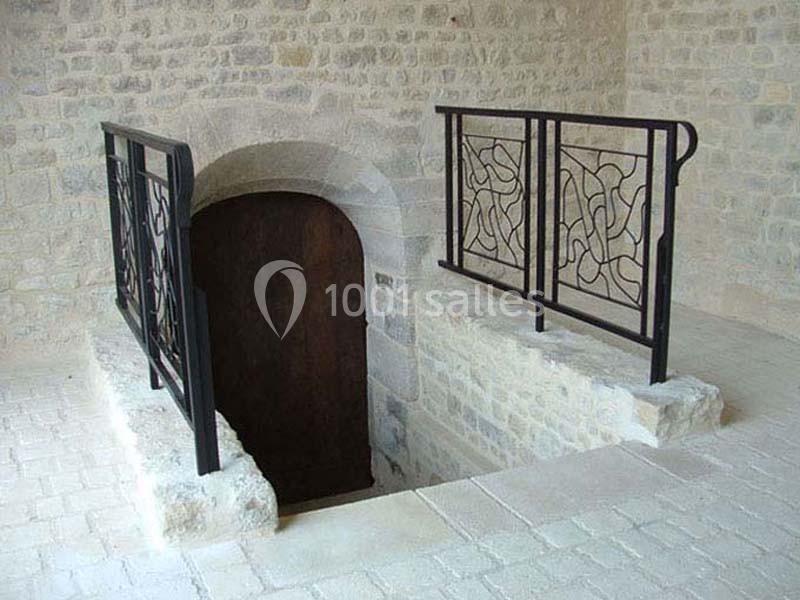 Escalier en pierre descendant vers une porte en bois, encadré par des garde-corps en métal noir au design abstrait.