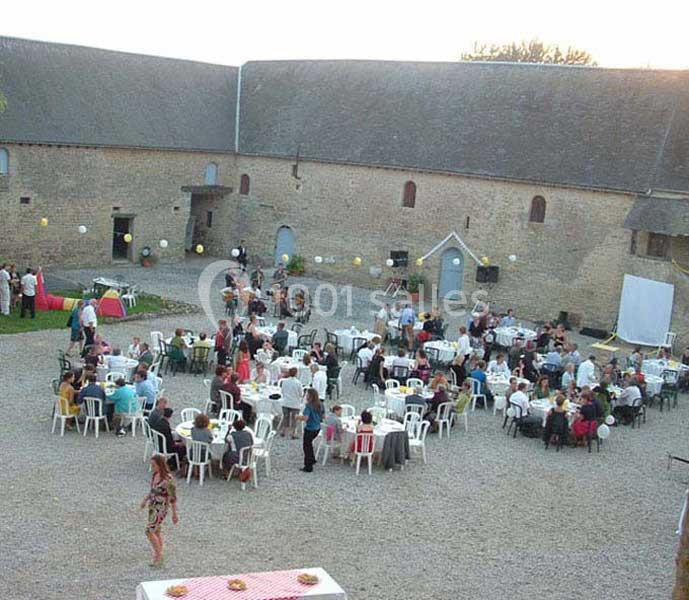 Personnes assises à des tables rondes dans une cour pavée entourée de bâtiments en pierre, lors d'un événement en plein air.