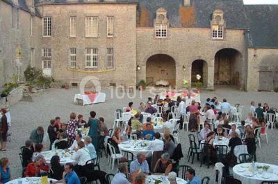 Cuisine rustique avec évier double, plan de travail en inox, réfrigérateur, cuisinière et mur en pierre apparente.