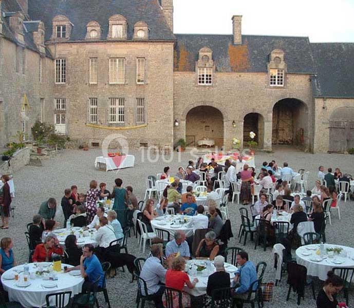 Groupe de personnes dînant à l'extérieur dans une cour pavée entourée de bâtiments anciens en pierre.