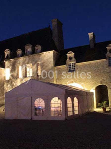 Tente blanche éclairée installée devant un bâtiment en pierre illuminé, de nuit.