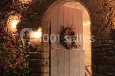 Cuisine rustique avec évier double, plan de travail en inox, réfrigérateur, cuisinière et mur en pierre apparente.