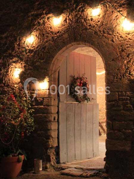 Porte en bois ouverte dans un mur en pierre, décorée d'une couronne et entourée de guirlandes lumineuses.