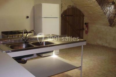 Cuisine rustique avec évier double, plan de travail en inox, réfrigérateur, cuisinière et mur en pierre apparente.