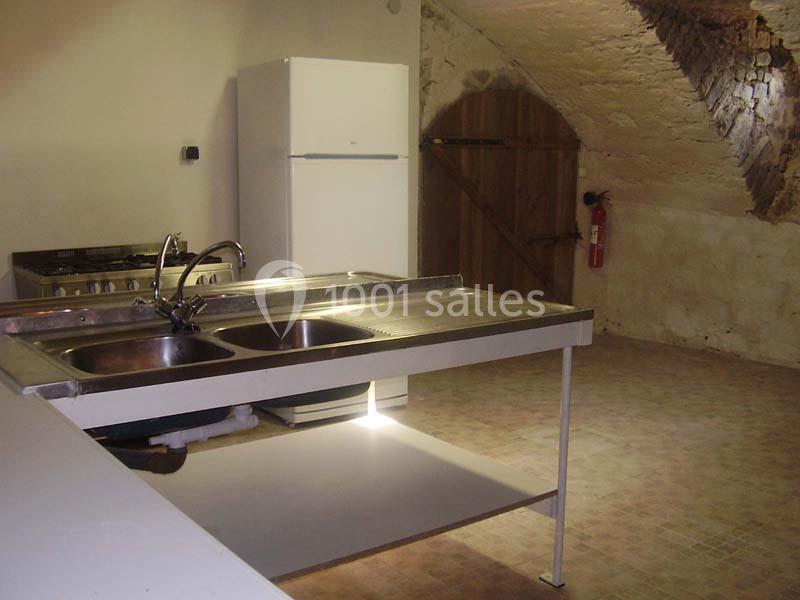 Cuisine rustique avec évier double, plan de travail en inox, réfrigérateur, cuisinière et mur en pierre apparente.