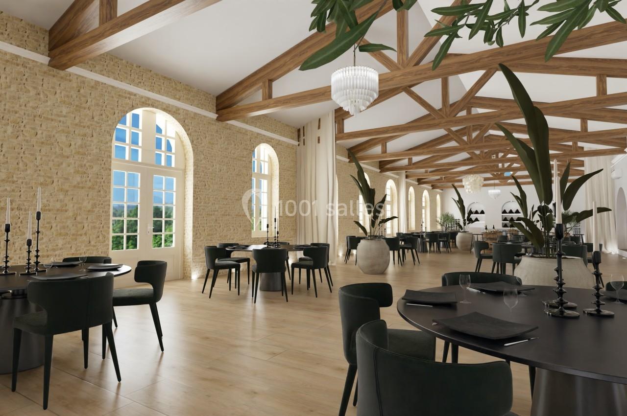 Salle lumineuse avec murs en pierre, grandes fenêtres cintrées, poutres apparentes et tables élégamment dressées.