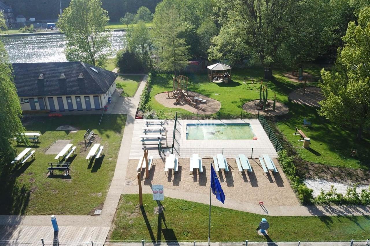 Vue aérienne d'un espace extérieur avec piscine, tables de pique-nique, aire de jeux et bâtiments entourés de verdure.