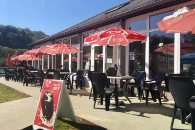 Aire de jeux en bois sur un sol sablé, entourée de verdure et située près d'une rivière et de collines.
