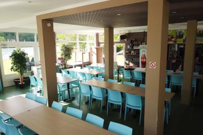 Aire de jeux en bois sur un sol sablé, entourée de verdure et située près d'une rivière et de collines.