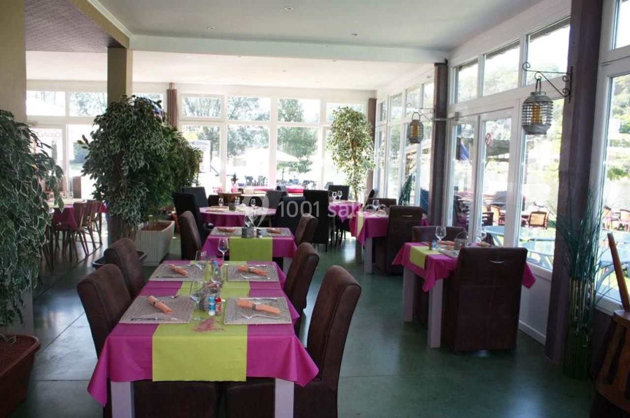 Salle de restaurant lumineuse avec tables dressées, nappes colorées et grandes baies vitrées donnant sur l'extérieur.