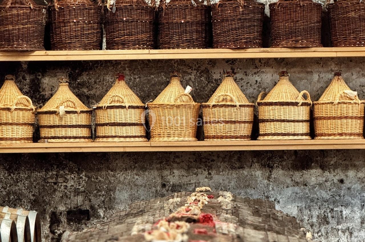 Des bouteilles en osier disposées sur des étagères en bois, dans un environnement rustique avec un mur en pierre.