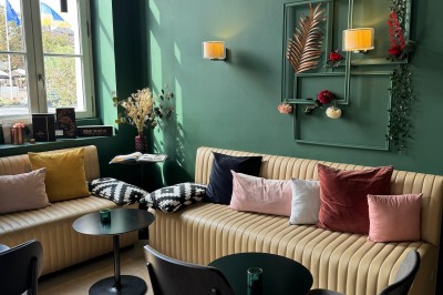 Intérieur d'un bar cosy avec un comptoir en bois, des tabourets hauts et des tables alignées dans un espace chaleureux.