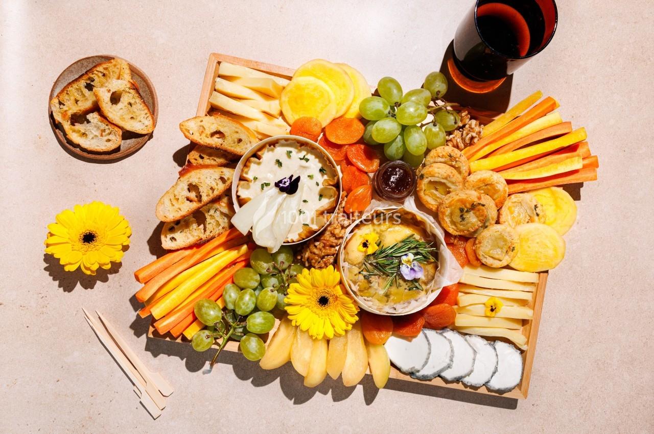 Plateau de fromages et légumes colorés avec fruits, pain, fleurs décoratives et un verre de vin rouge.