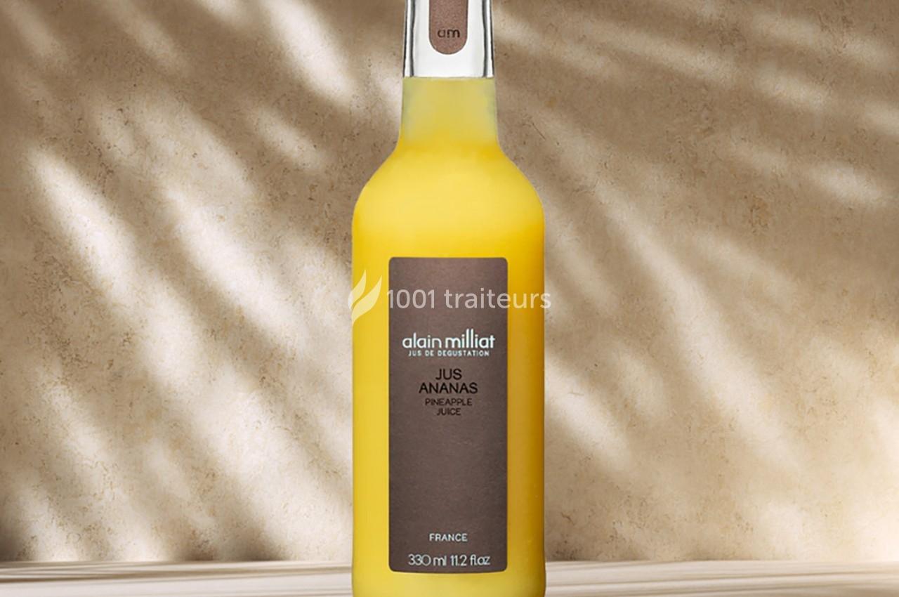 Bouteille de jus d'ananas avec étiquette marron, posée sur une surface beige éclairée par une lumière tamisée.
