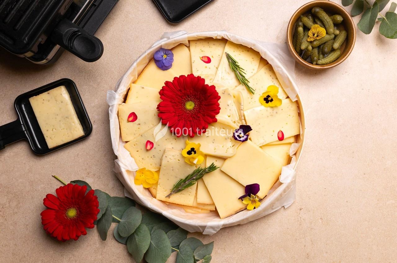 Plateau de fromage décoré de fleurs comestibles, accompagné de cornichons et d'un appareil à raclette.