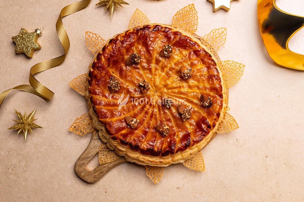 Galette des rois dorée sur une planche en bois, décorée de noix et entourée d'éléments festifs dorés.