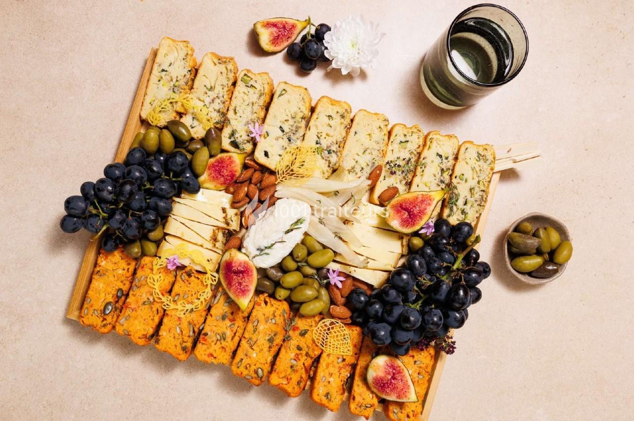 Plateau de fromages variés avec figues, raisins, olives, amandes et pain, accompagné d'un verre de vin blanc.