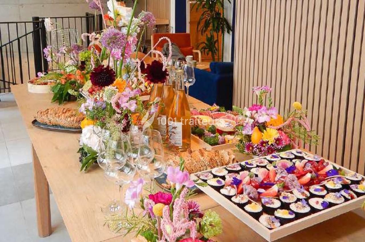 Table garnie de fleurs, bouteilles, verres et plats variés, dont des amuse-bouches et desserts colorés.