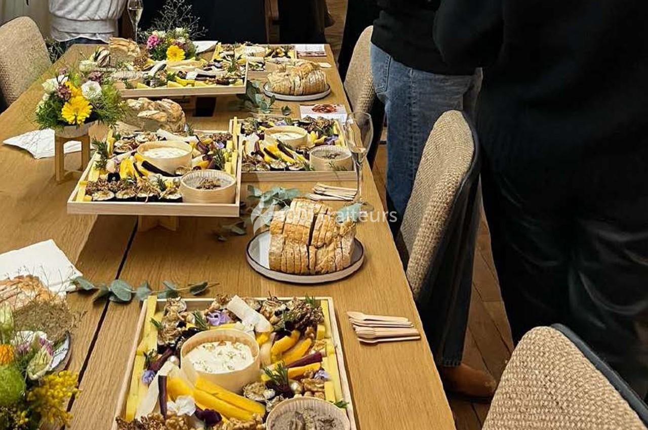 Plateaux de fromages et charcuteries disposés sur une table en bois, entourés de convives debout.