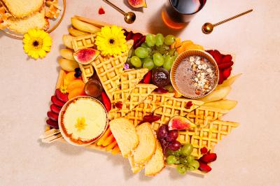 Plateau coloré de crudités, fromages, dips, fruits secs et fleurs comestibles disposés de manière artistique.