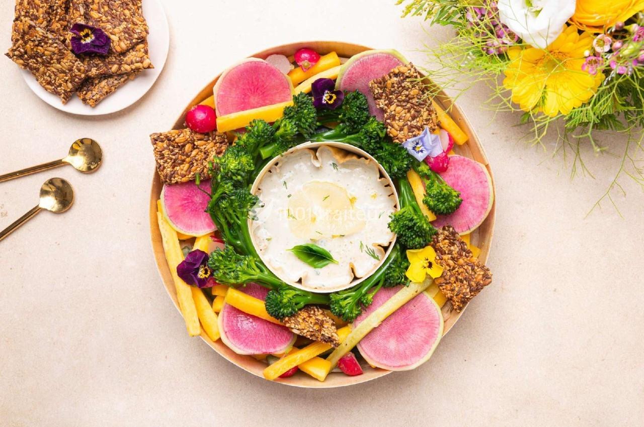 Plateau de légumes colorés avec dip au centre, entouré de crackers et décoré de fleurs comestibles.