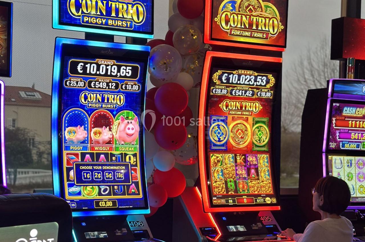 Deux machines à sous lumineuses avec écrans colorés, une personne assise devant l'une d'elles dans un casino.