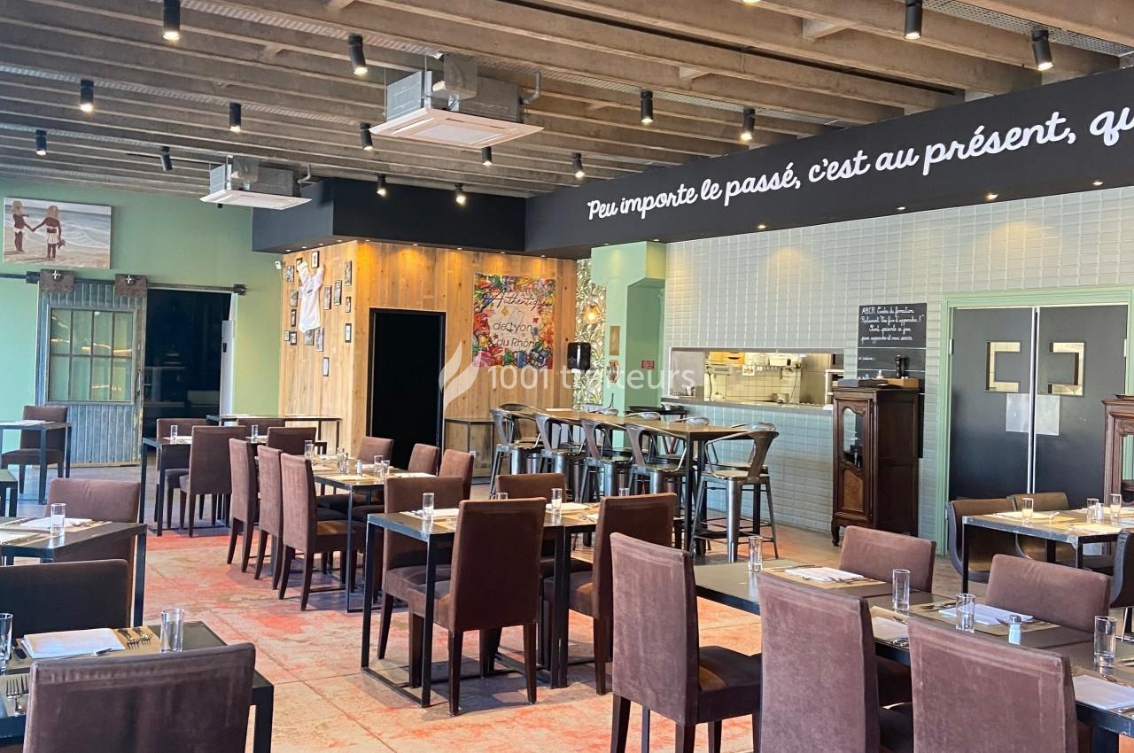 Salle de restaurant lumineuse avec tables dressées, chaises marron, bar en bois et décorations murales variées.