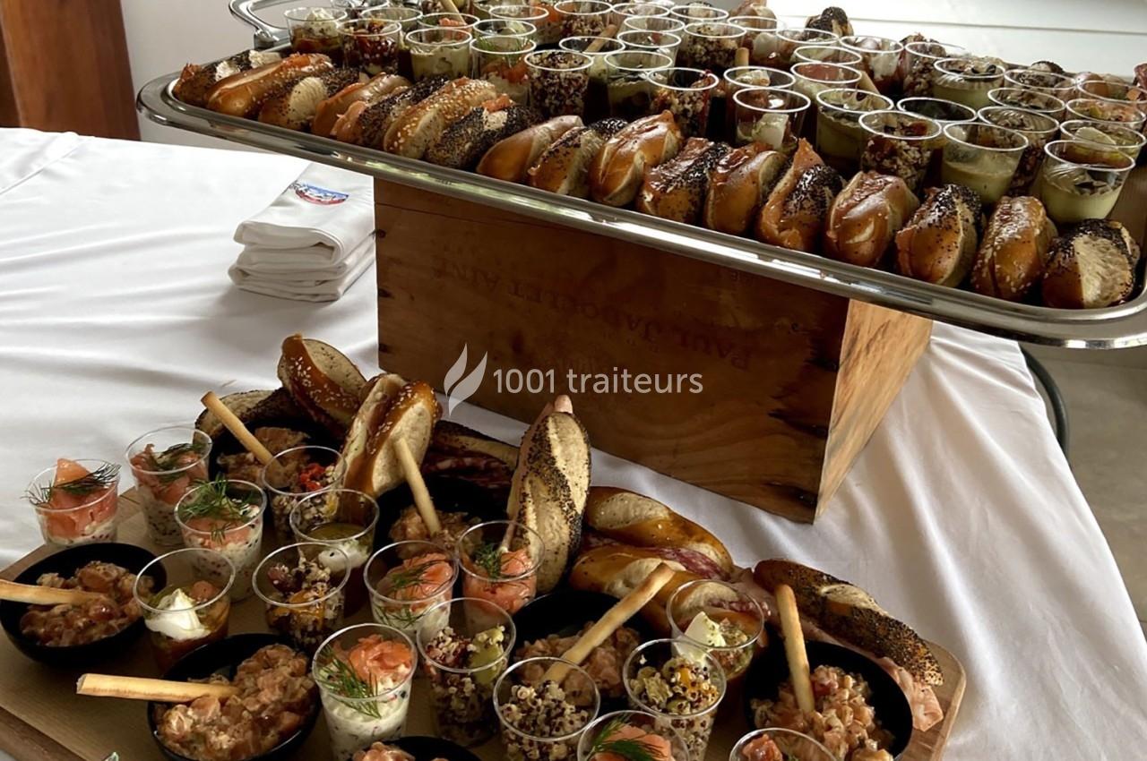 Plateau de buffet avec bagels variés et verrines garnies de préparations salées sur une nappe blanche.