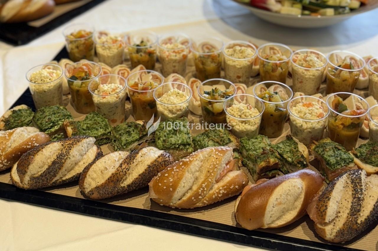 Plateau de buffet avec pains variés, verrines de salades et portions de quiches aux légumes.