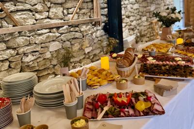 Table garnie de plats variés, incluant charcuterie, pains, légumes et desserts, disposée devant un mur en pierre.